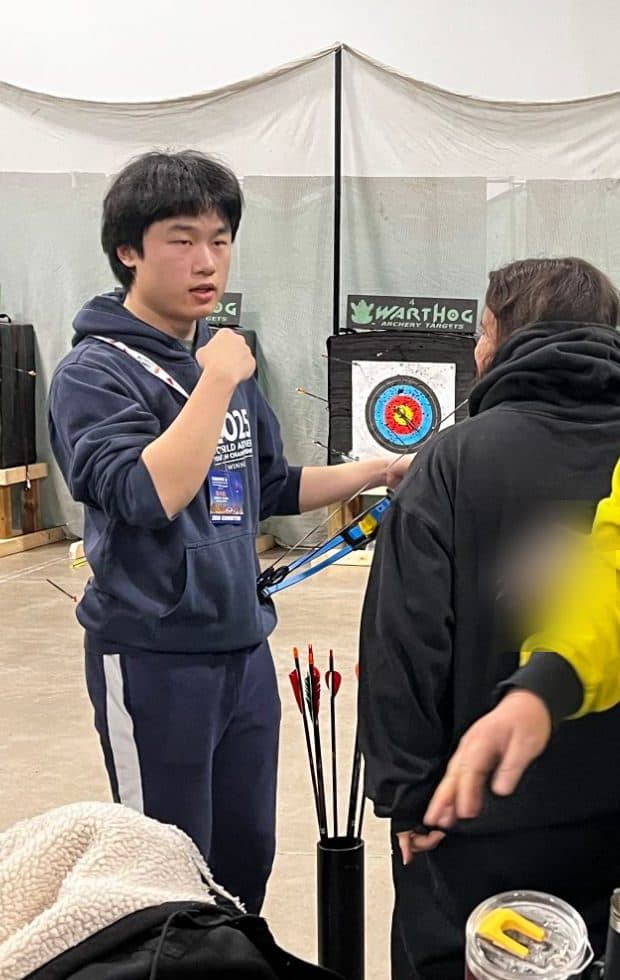 A founder coaching an archer at an indoor range. The archer is seen from behind.